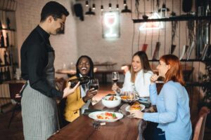 ragazze a tavola, cameriere versa vino